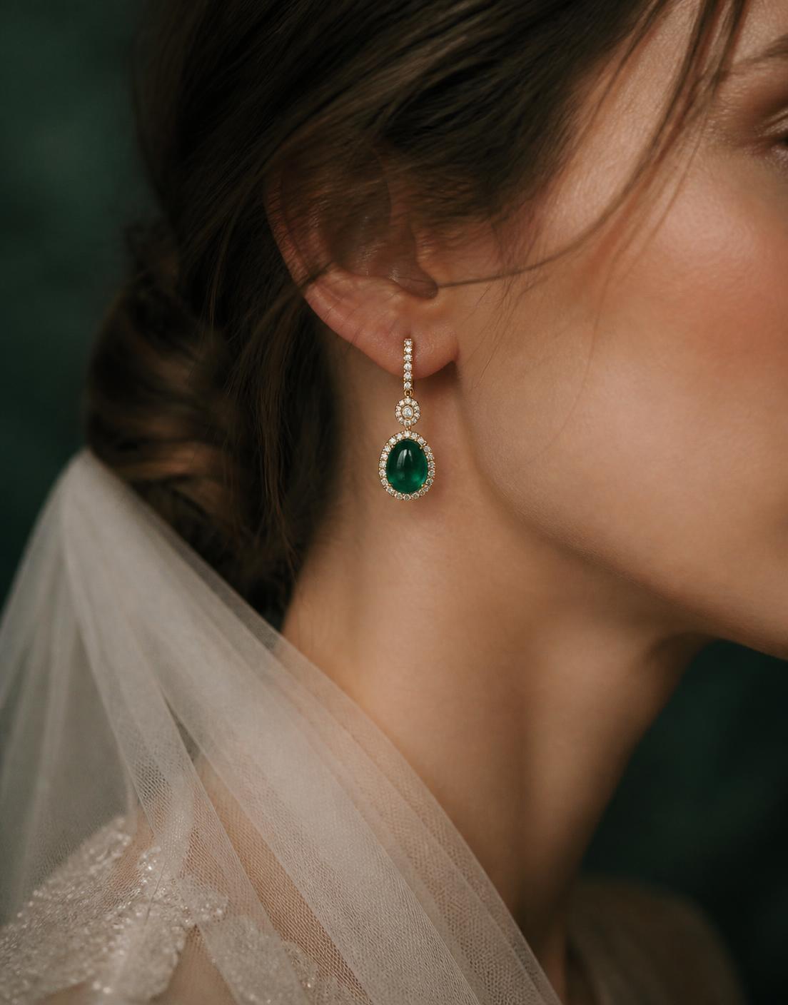 Bride wearing a long emerald and white gold drop earring beside an embroidered veil